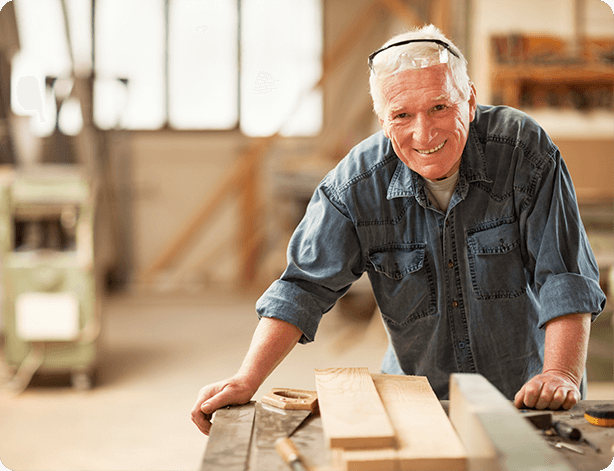 Old man smiling while doing some woodwork.